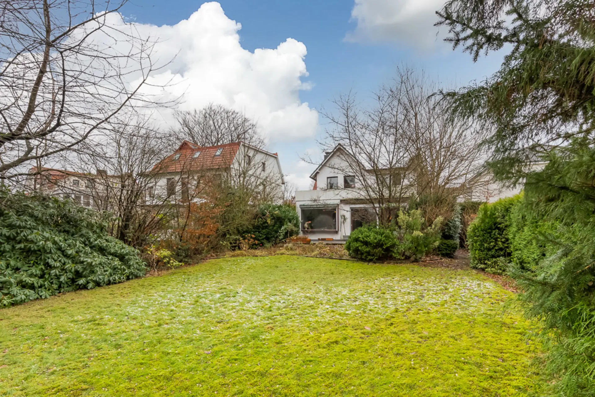 Großer Garten mit Rasenfläche, Büschen und Blick auf ein Wohnhaus im Hintergrund.