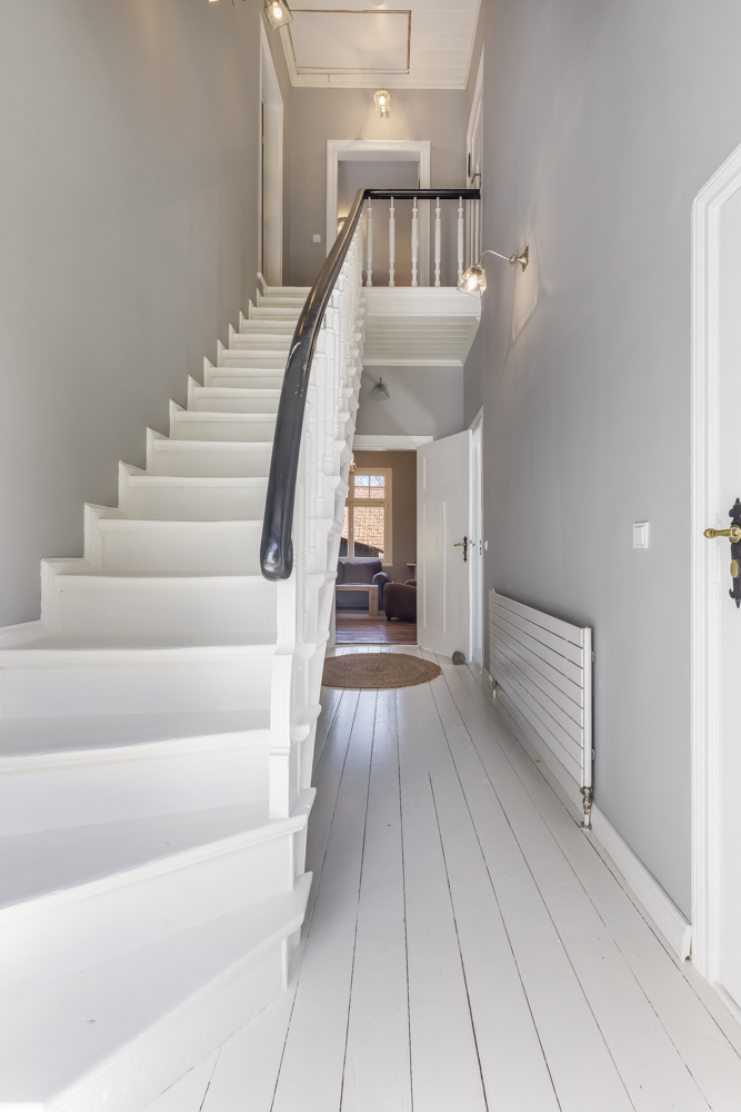 Heller Flur mit weißer Treppe, Holzboden und Blick in ein Wohnzimmer.