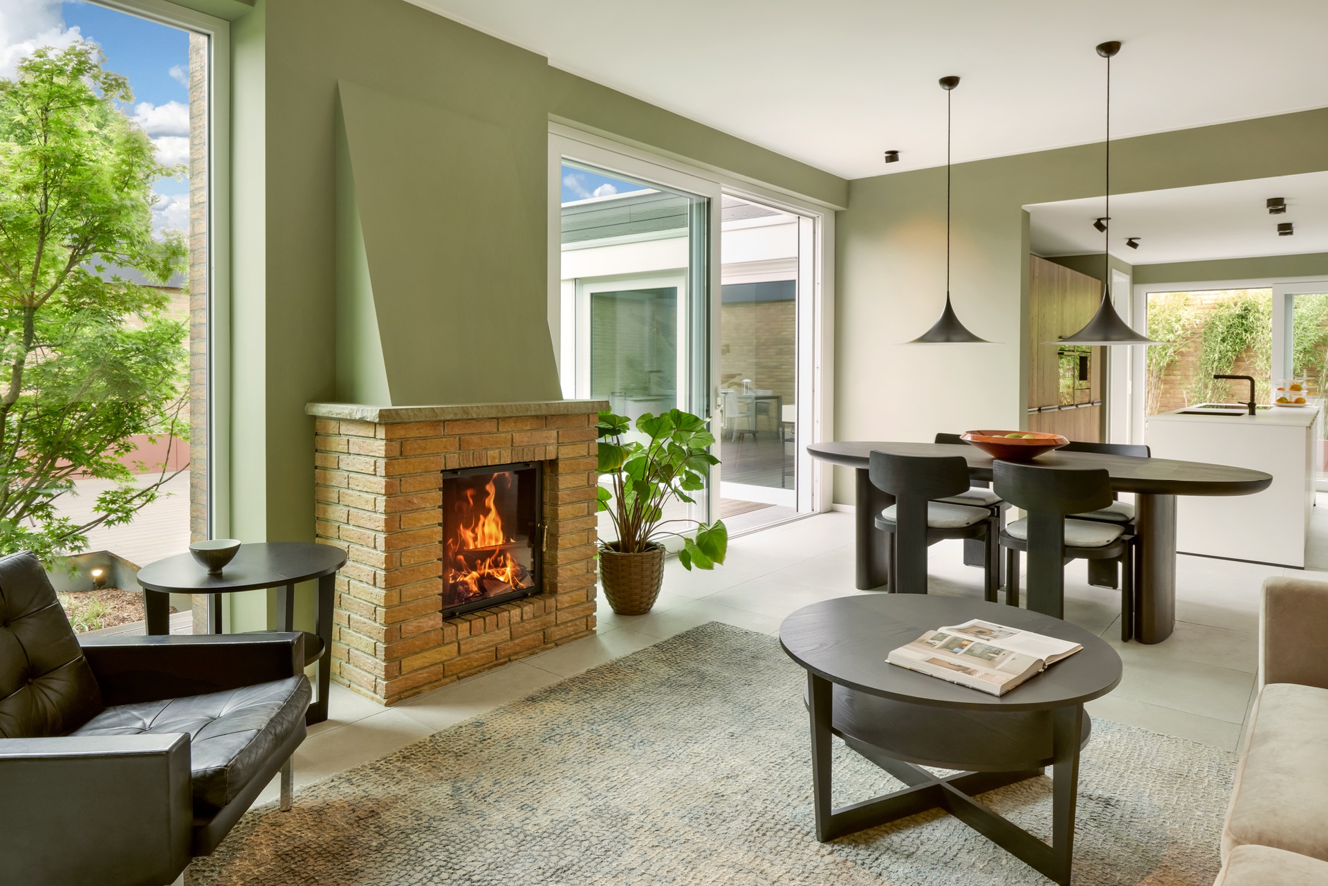 Modernes Wohnzimmer mit Kamin, runden Tischen, Sesseln und großen Fenstern zum Garten.