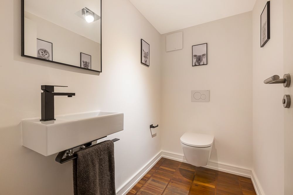 Modernes Gäste-WC mit Wandtoilette, kleinem Waschbecken, Spiegel und Tierbildern an weißen Wänden.