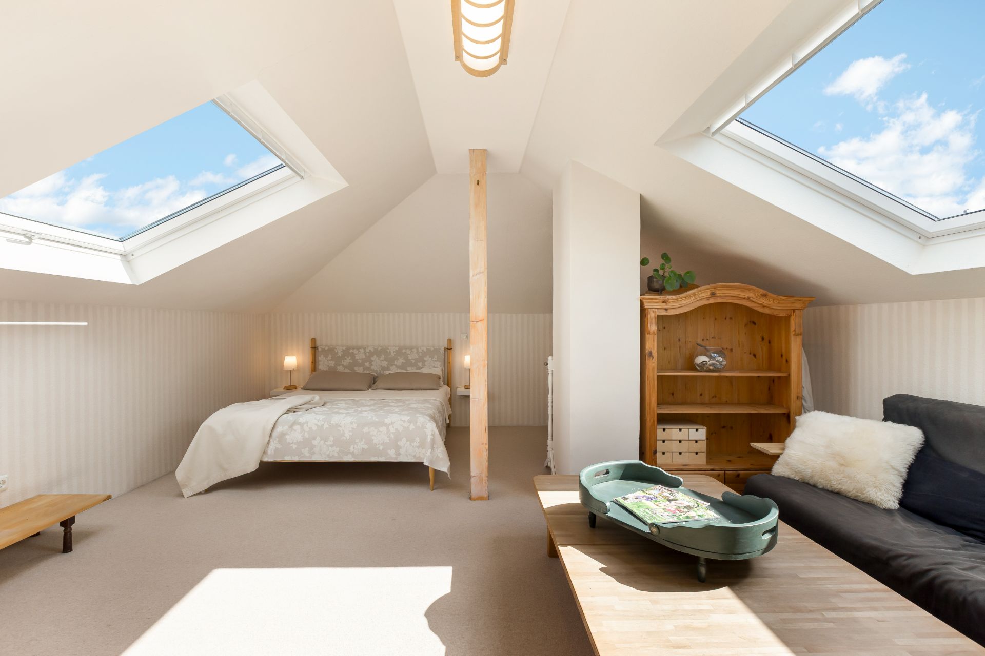 Helles Dachzimmer mit Bett, Sofa, Holztisch und Dachfenstern.