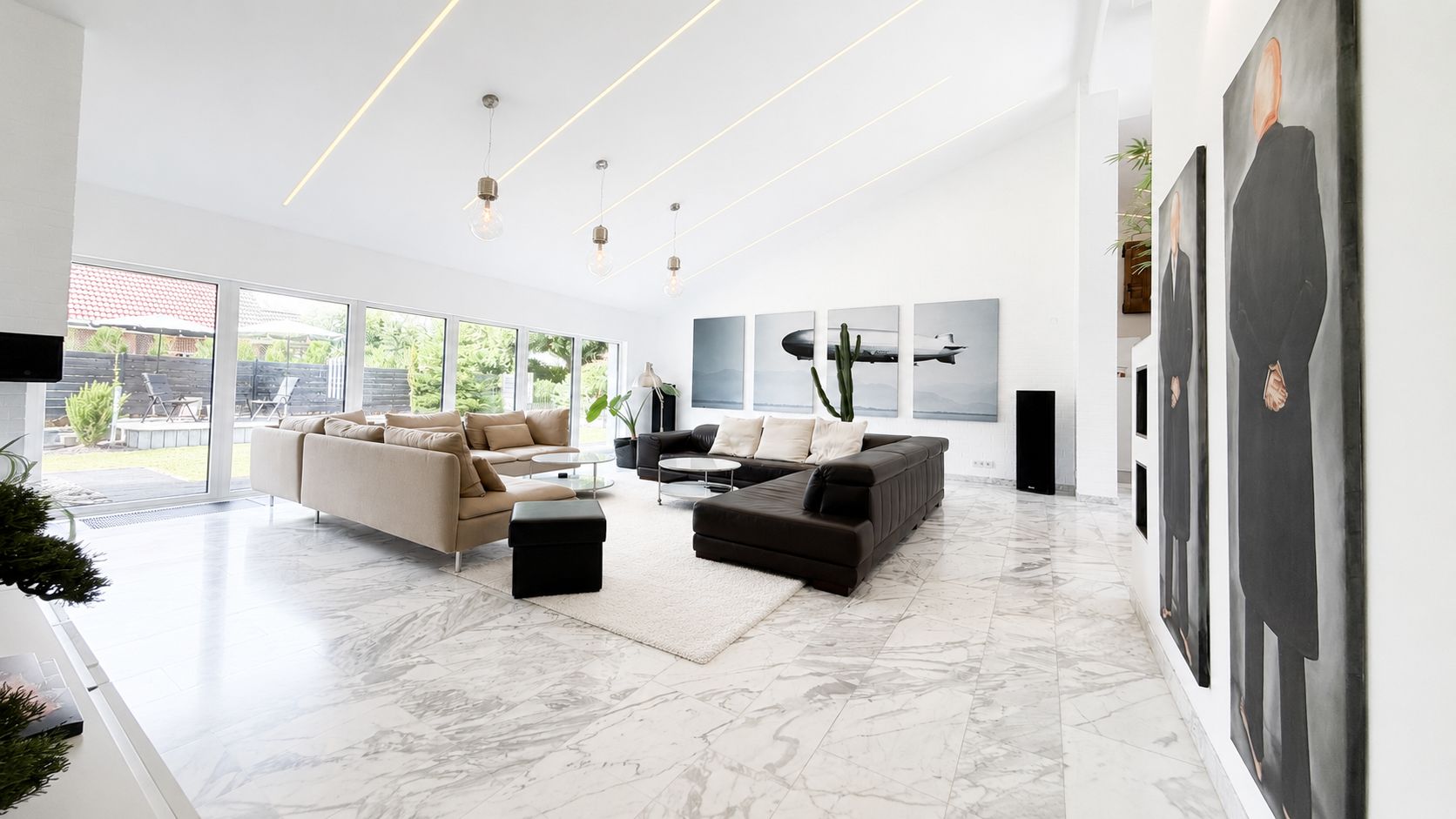 Helles Wohnzimmer mit großen Sofas, Marmorboden und großen Fenstern zum Garten.