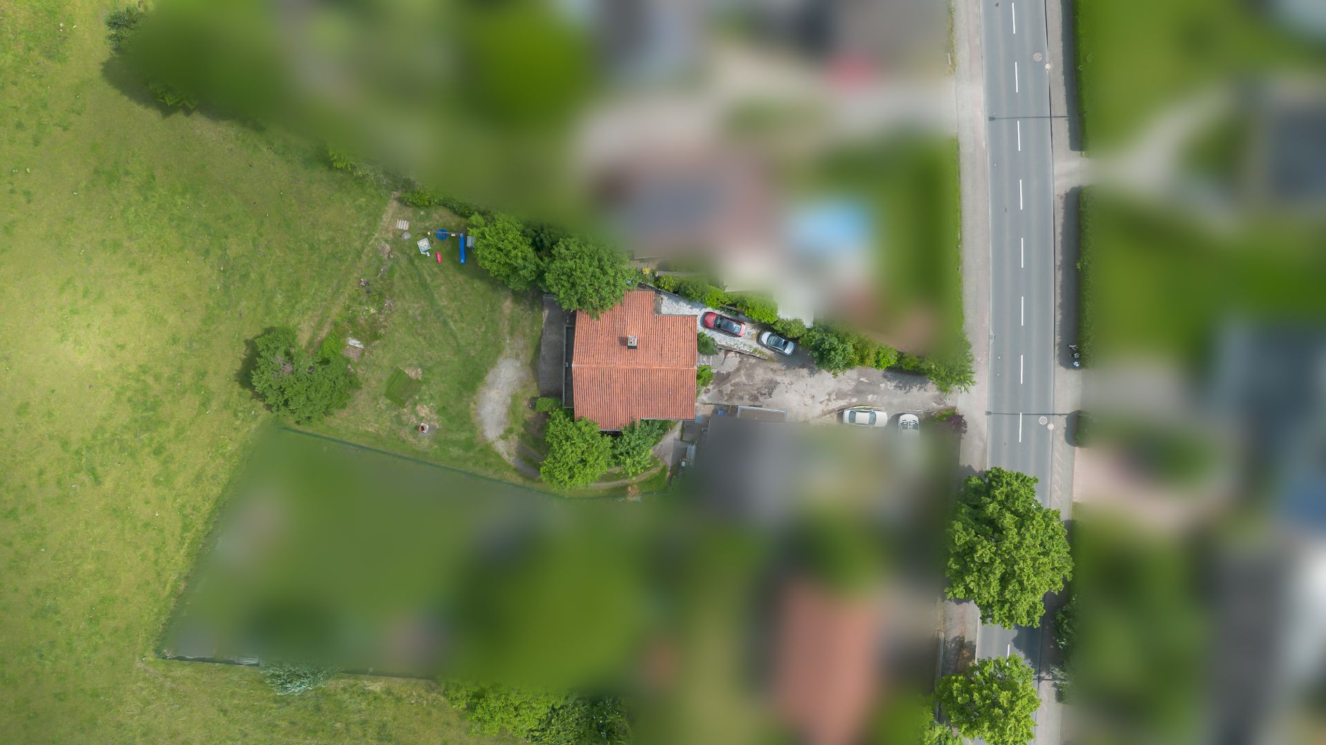 Luftaufnahme eines Hauses mit rotem Dach, großem Garten und angrenzender Straße.