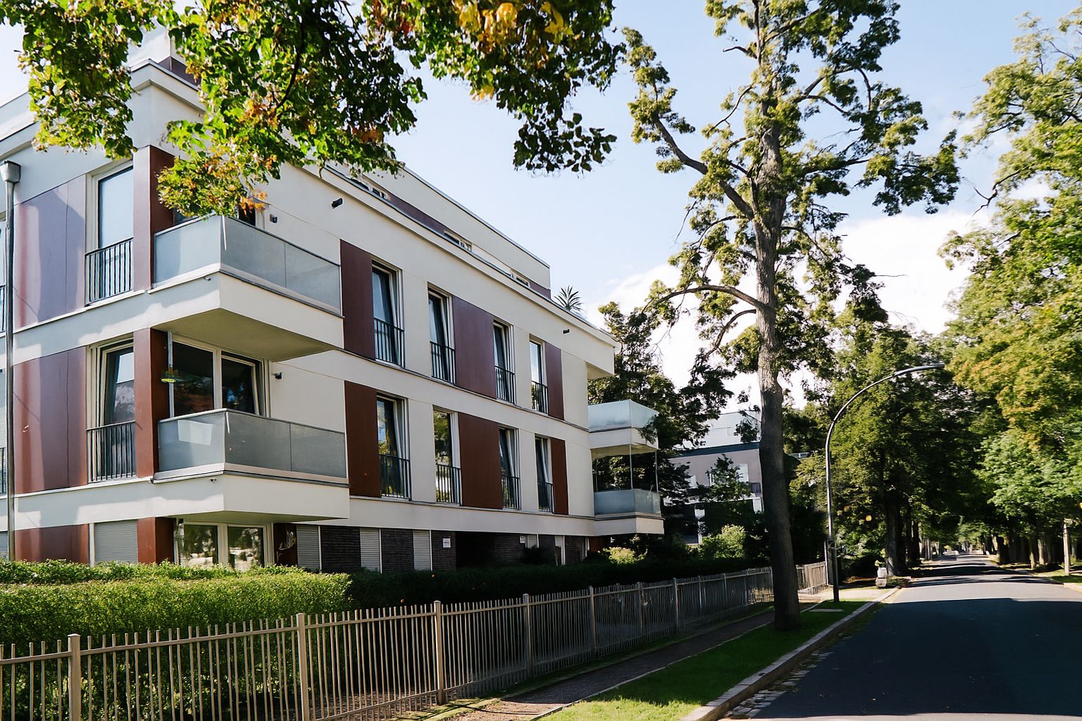 Modernes Wohngebäude mit Balkonen an einer von Bäumen gesäumten Straße.