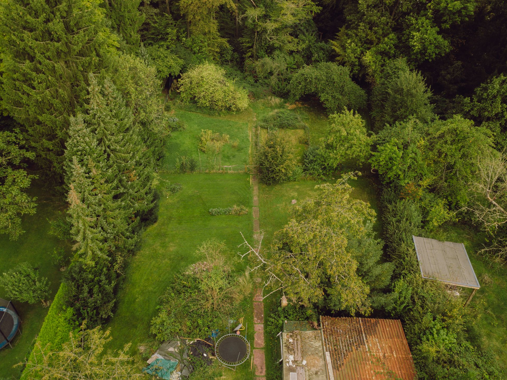 Luftaufnahme eines großen Gartens mit Bäumen, Rasen, Schuppen und einem Trampolin.