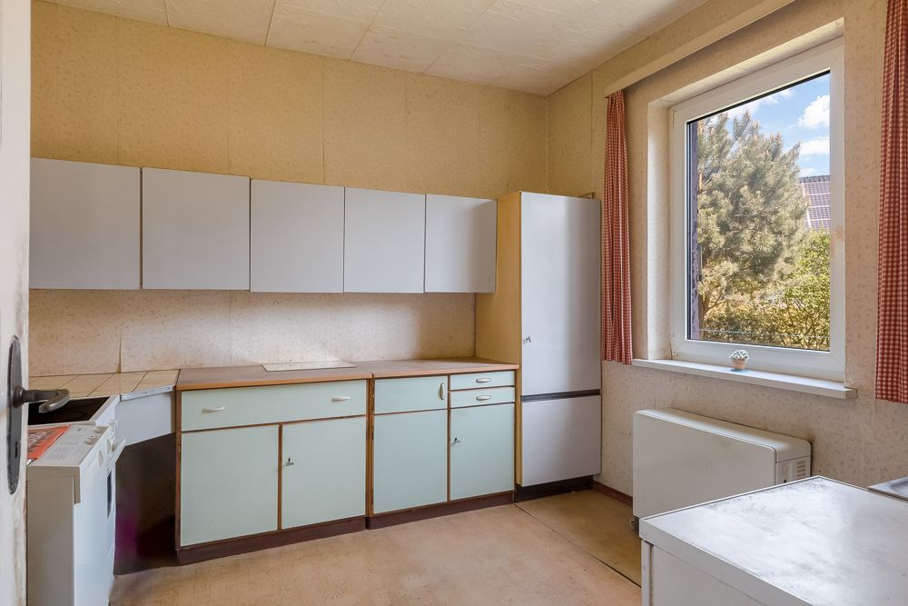 Helle Küche mit weißen Schränken, Kühlschrank und großem Fenster mit Blick ins Grüne.