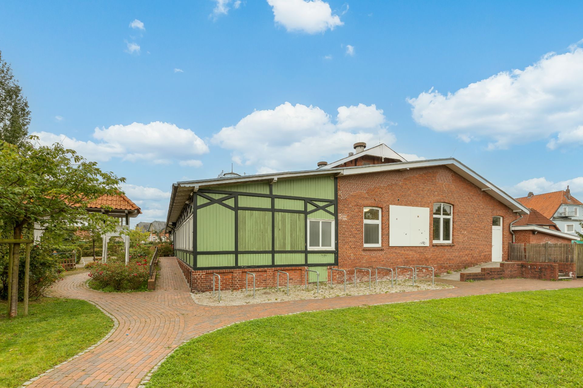 Backsteinwohnhaus mit Fachwerkelementen, grünem Tor und gepflegtem Gartenweg im Vordergrund.