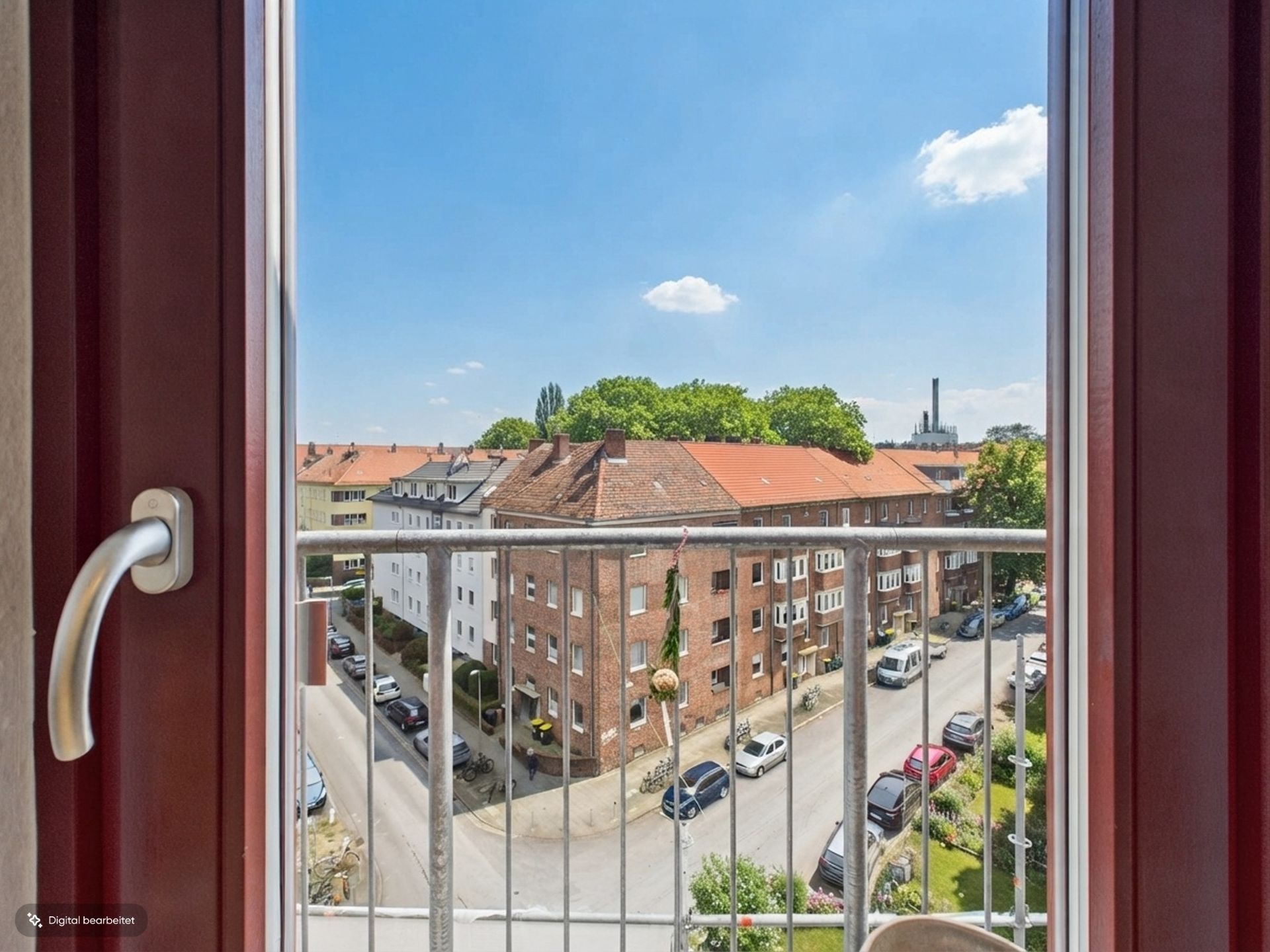 Blick aus einem Fenster auf einen Balkon, Wohnhäuser und eine Straße mit geparkten Autos.