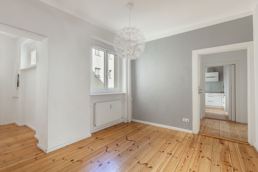 Heller Raum mit Holzfußboden, grauer Wand, Fenster und moderner Lampe.