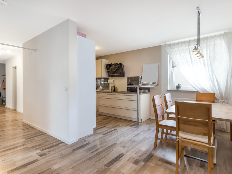 Moderne Küche und Essbereich mit Holzboden, Holztisch und Stühlen, Fenster mit Vorhang rechts.