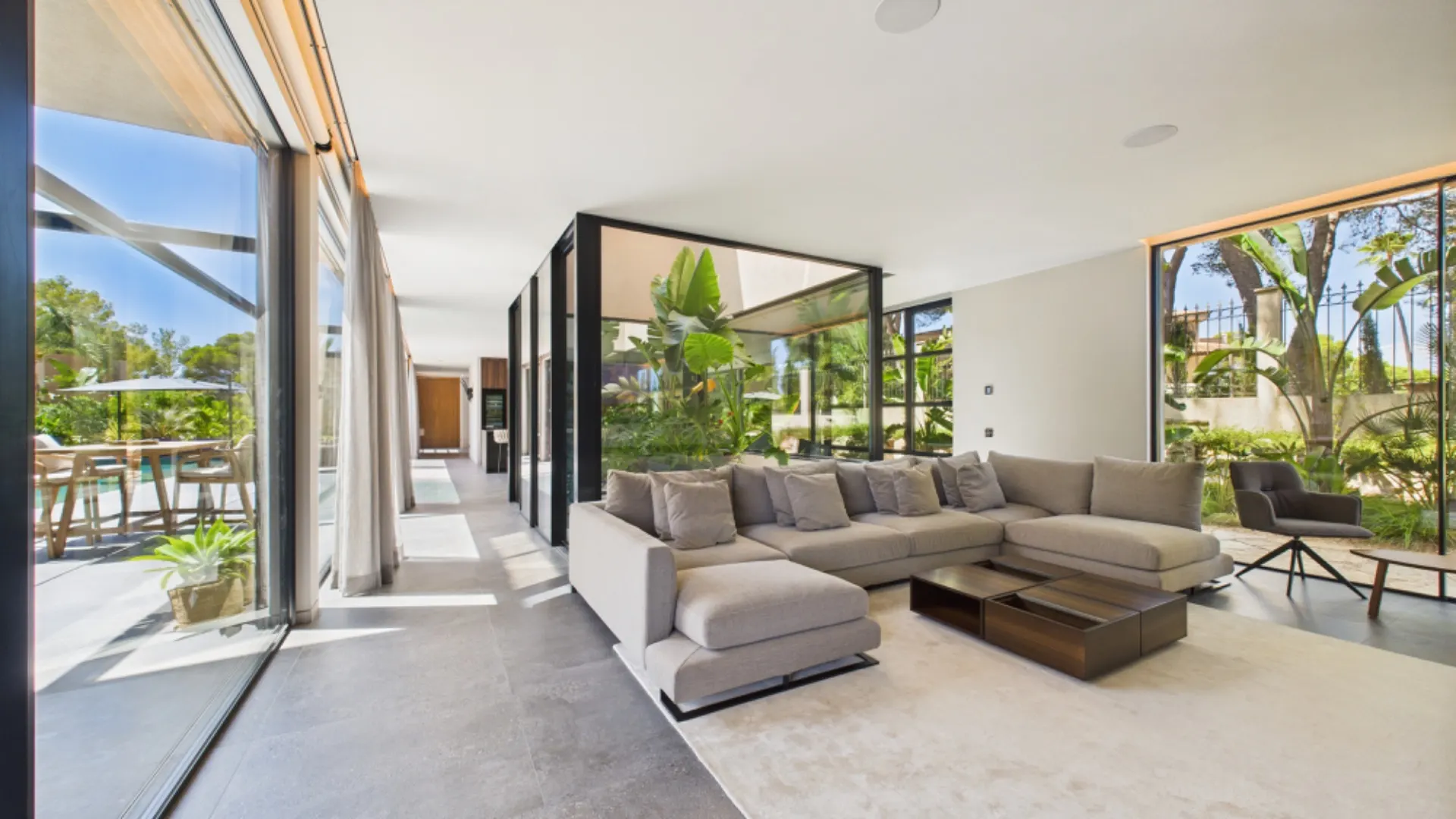Modernes Wohnzimmer mit großem Ecksofa und großen Fenstern, Blick auf Garten mit Pflanzen.
