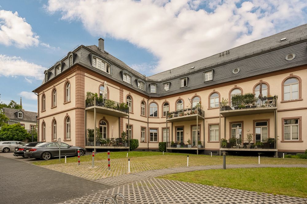 Großes Wohngebäude mit Balkonen, gepflegtem Rasen und geparkten Autos davor.