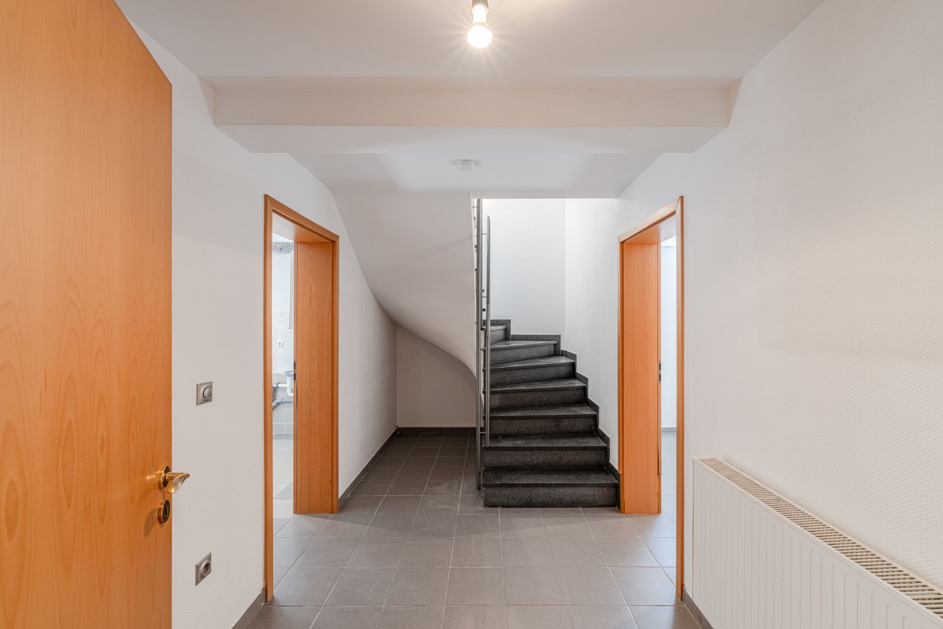 Heller Flur mit grauen Fliesen, zwei Türen und einer Treppe nach oben.