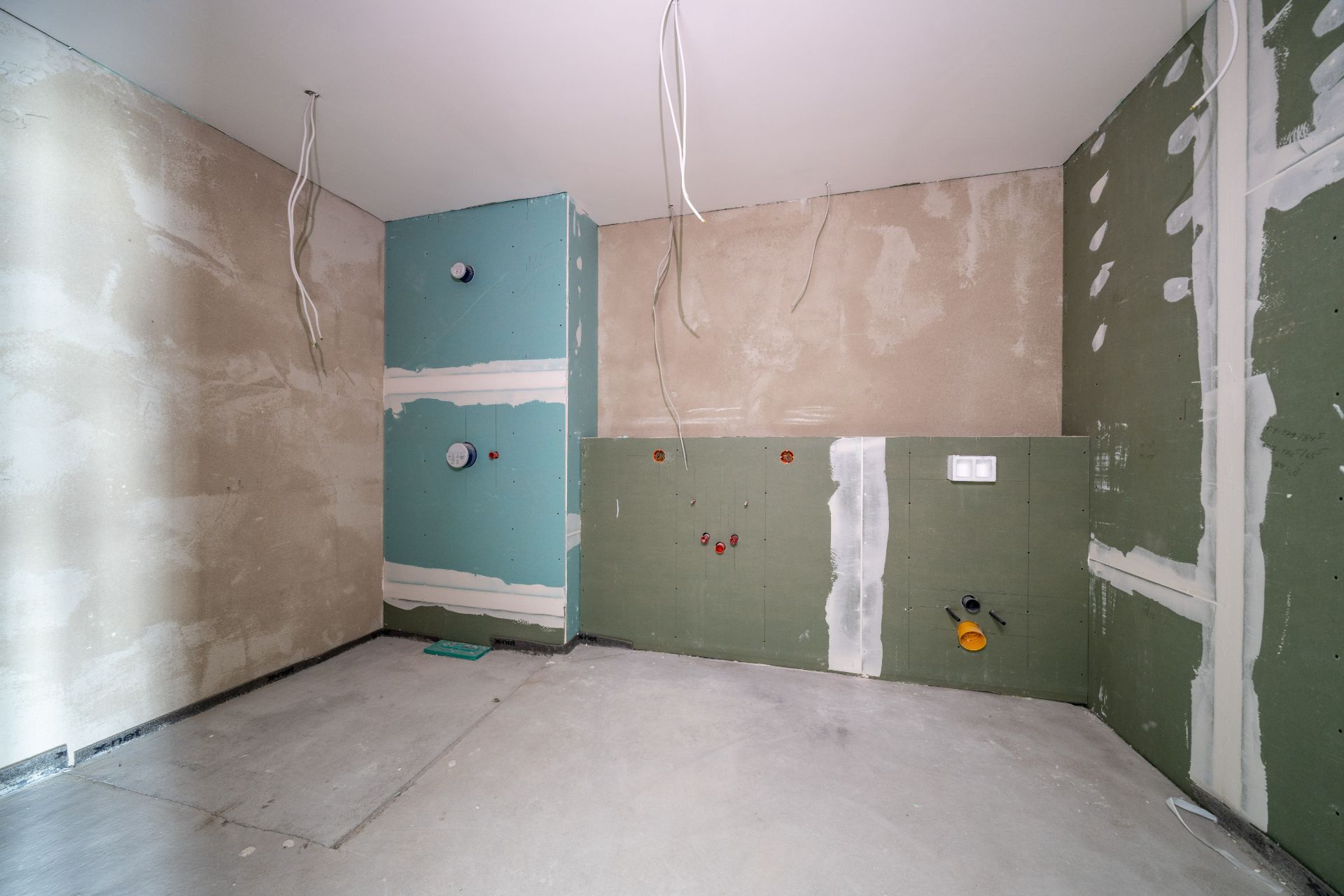 Unfertiger Raum mit grünen und beigen Wänden, sichtbaren Leitungen und Kabeln an Decke und Wänden.