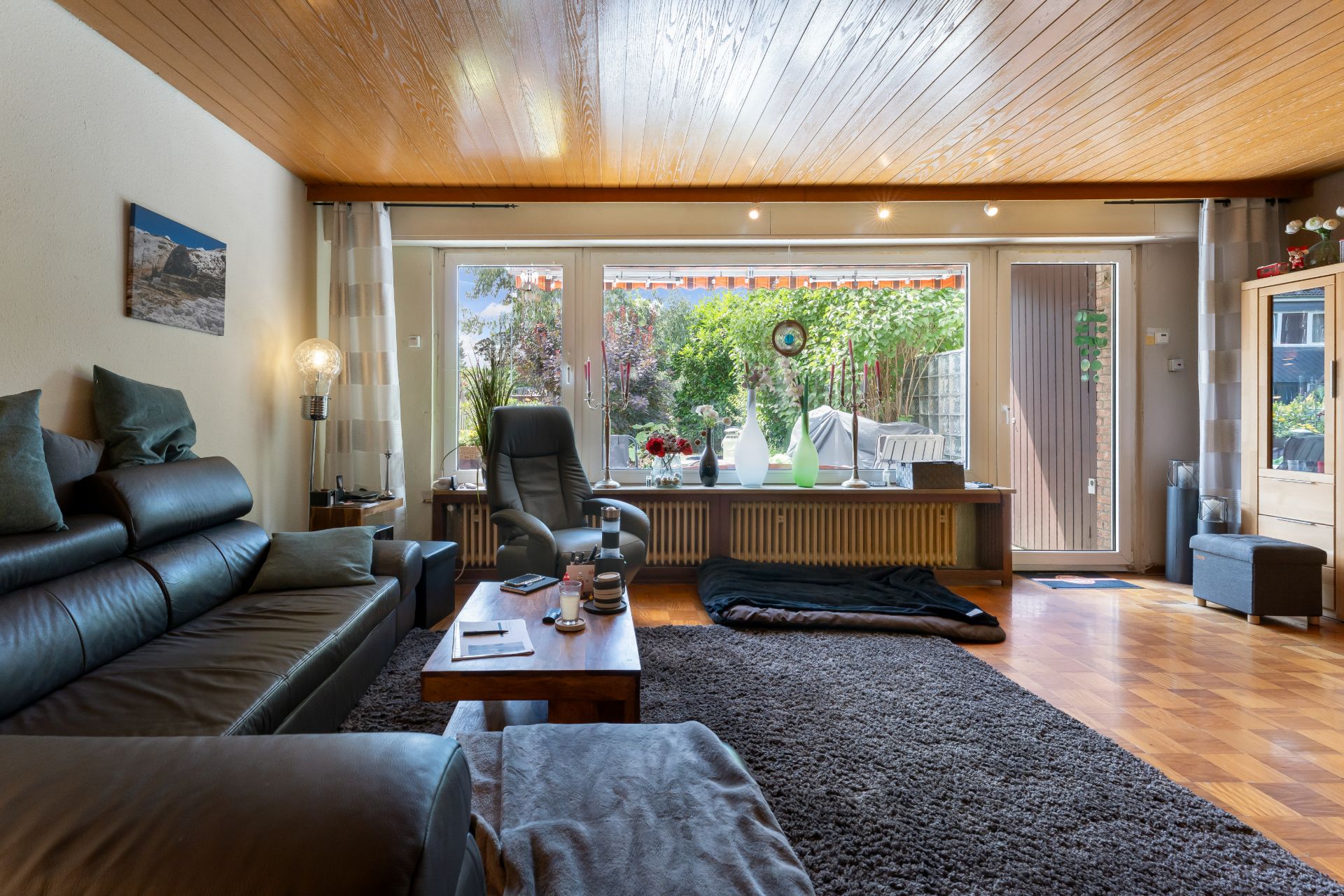 Helles Wohnzimmer mit Ledersofa, Sessel, Couchtisch und großem Fenster mit Blick in den Garten.