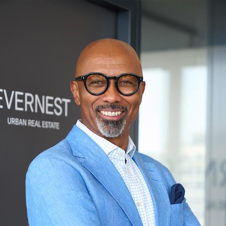 Ein lächelnder Mann mit Brille und blauem Sakko steht vor einer Glastür.