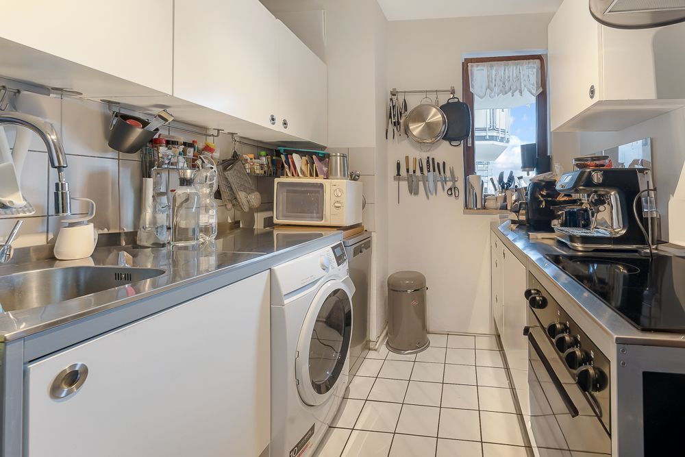 Moderne, schmale Küche mit Waschmaschine, Herd, Spüle und Küchenutensilien an den Wänden.