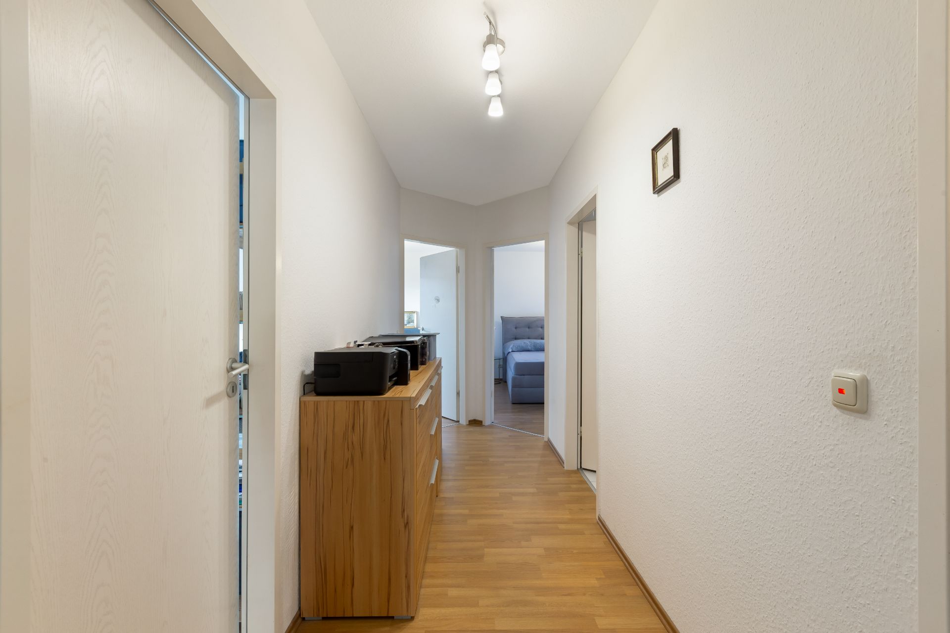Heller Flur mit Holzkommode und Türen zu weiteren Räumen, Holzboden und Deckenleuchte.