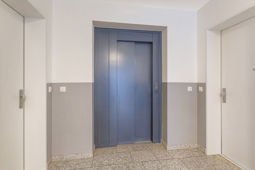 Flur mit Aufzugtür in der Mitte und zwei weißen Wohnungstüren an den Seiten.