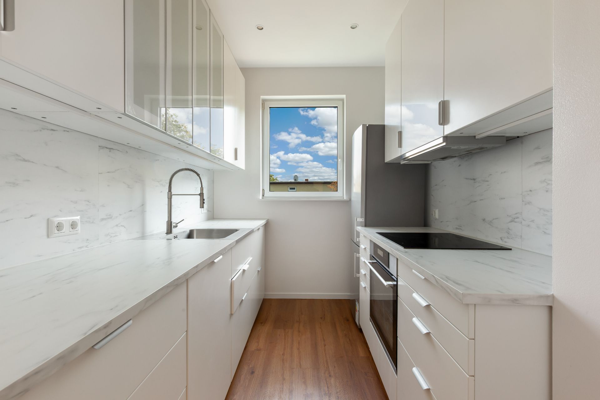 Moderne Einbauküche mit weißen Schränken, Holzfußboden und Fenster mit Ausblick.