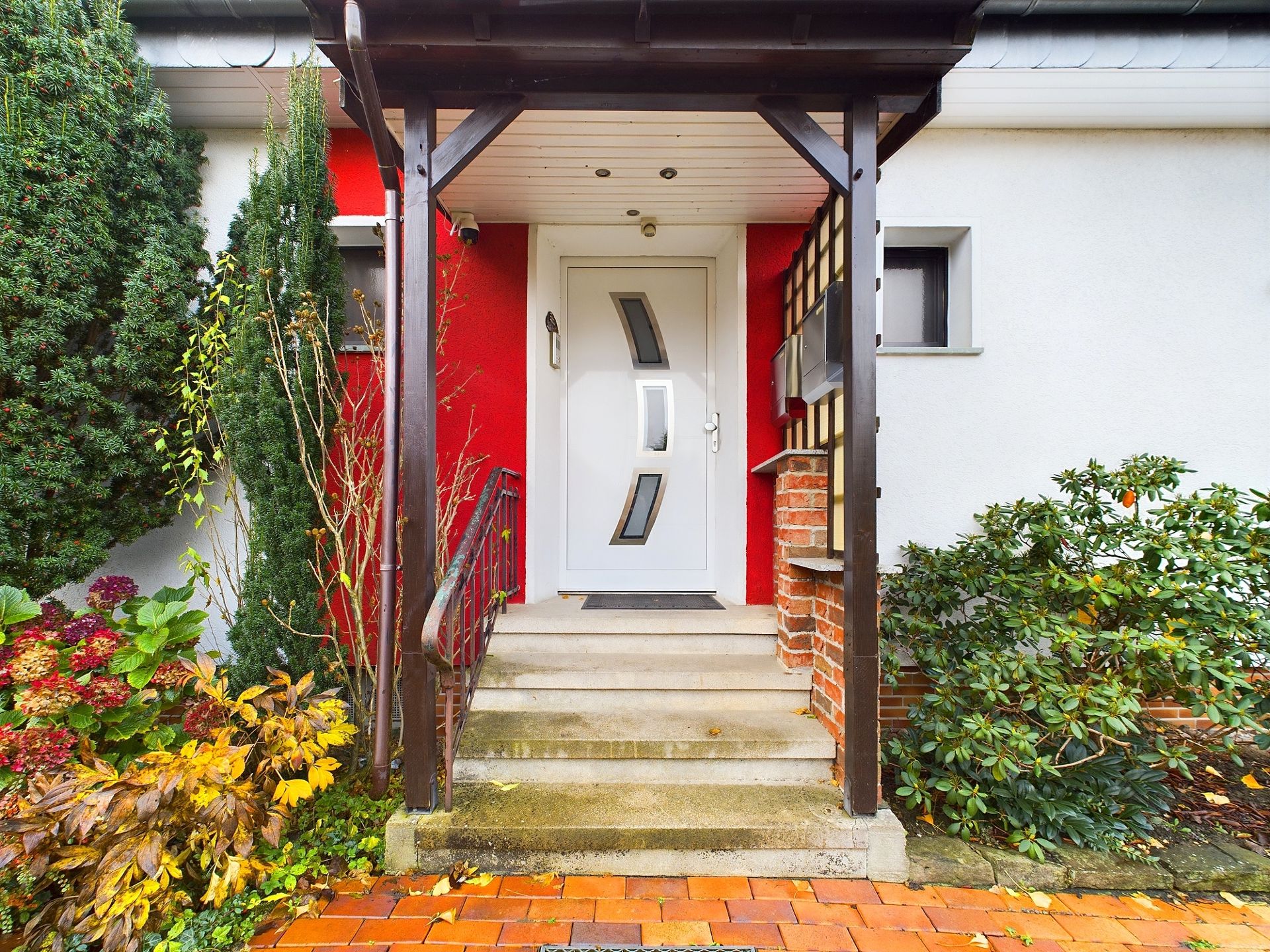 Eingangstür eines Hauses mit Vordach, Treppe und Pflanzen an beiden Seiten.