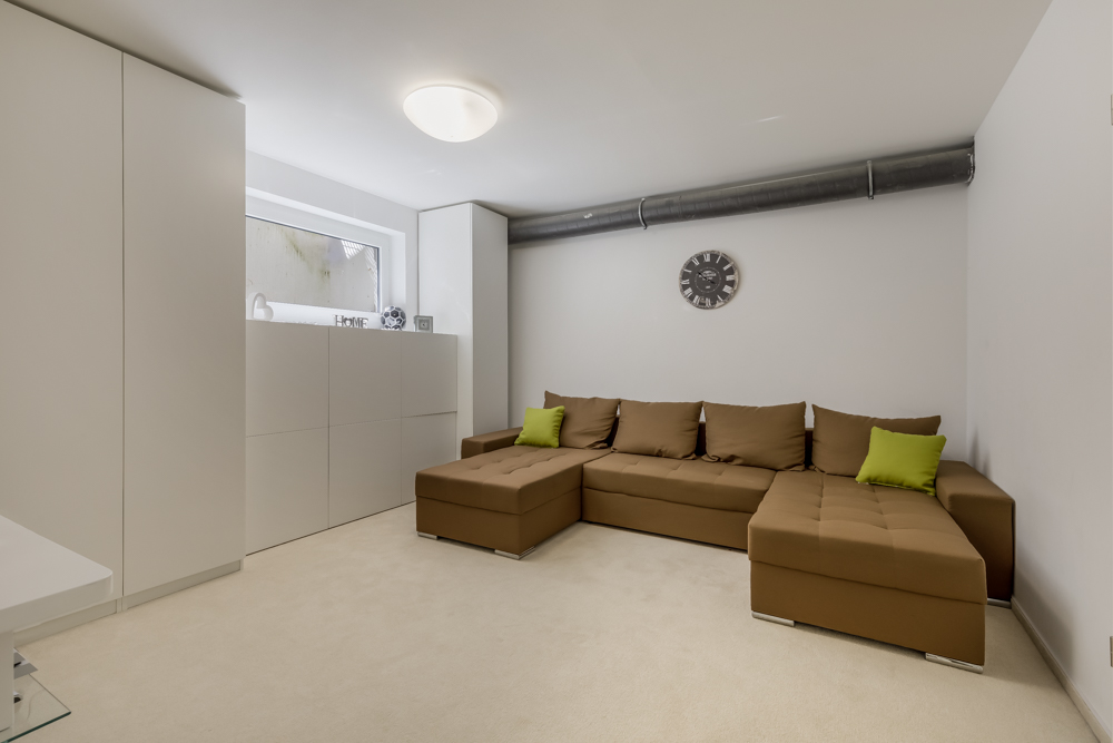 Heller Raum mit braunem Ecksofa, weißen Schränken und Wanduhr.