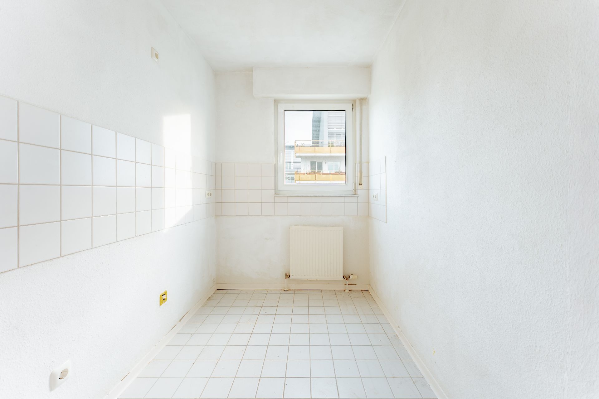 Heller, leerer Raum mit weißen Fliesen, Fenster und Heizkörper.