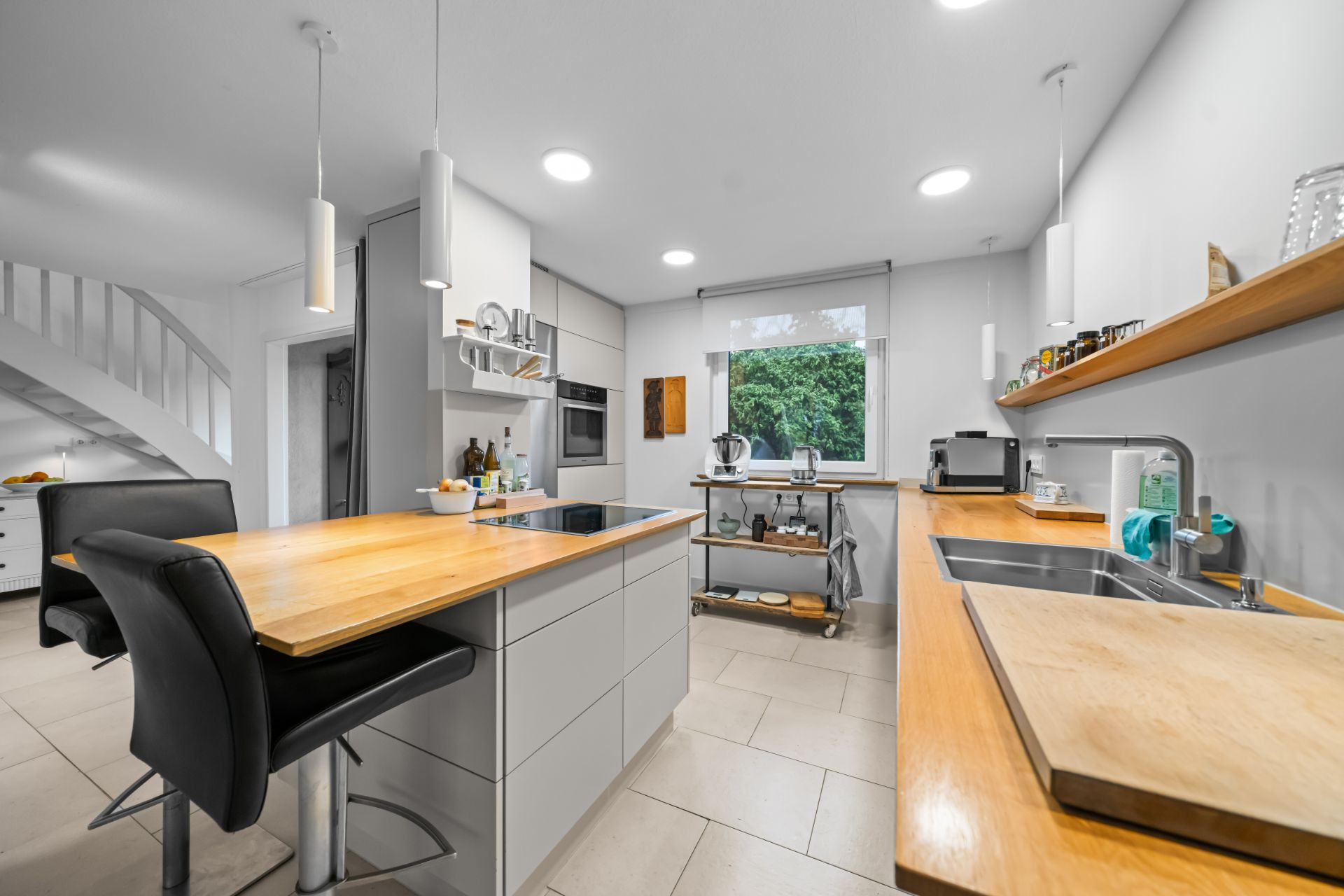 Moderne Küche mit Kochinsel, Holzarbeitsplatten, Spüle, Fenster und weißen Wänden.