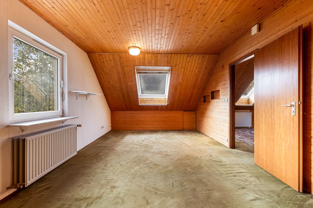 Leeres Dachzimmer mit Holzdecke, Teppichboden, Fenster und offenstehender Tür.