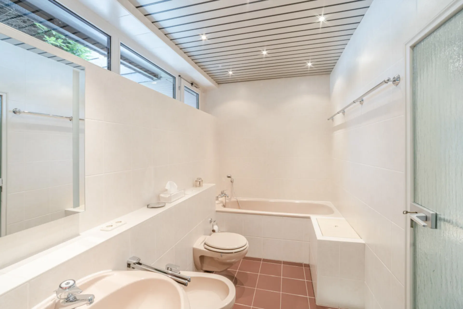 Helles Badezimmer mit Badewanne, Waschbecken, WC und großen Fenstern.