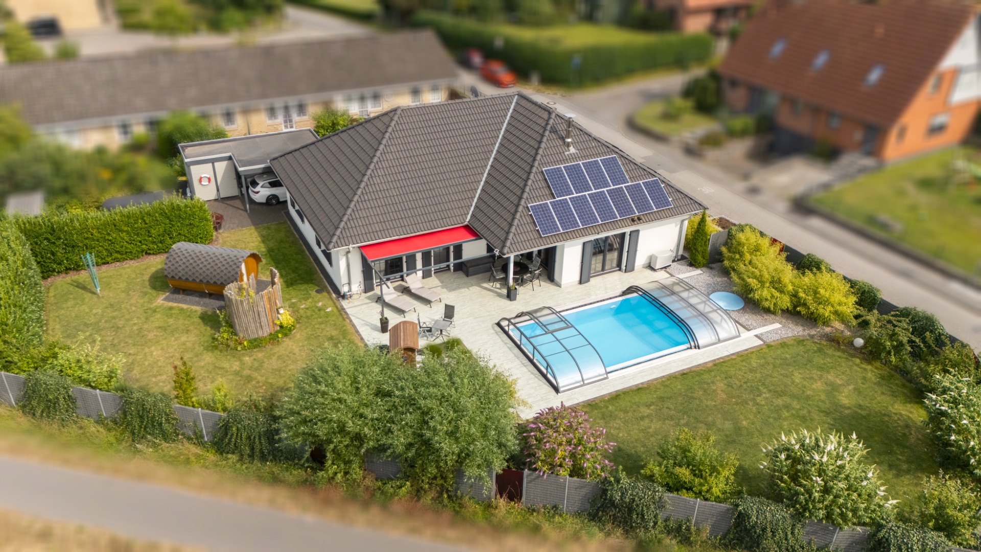 Modernes Haus mit Garten, Terrasse, Pool mit Überdachung und Solarpanelen auf dem Dach.