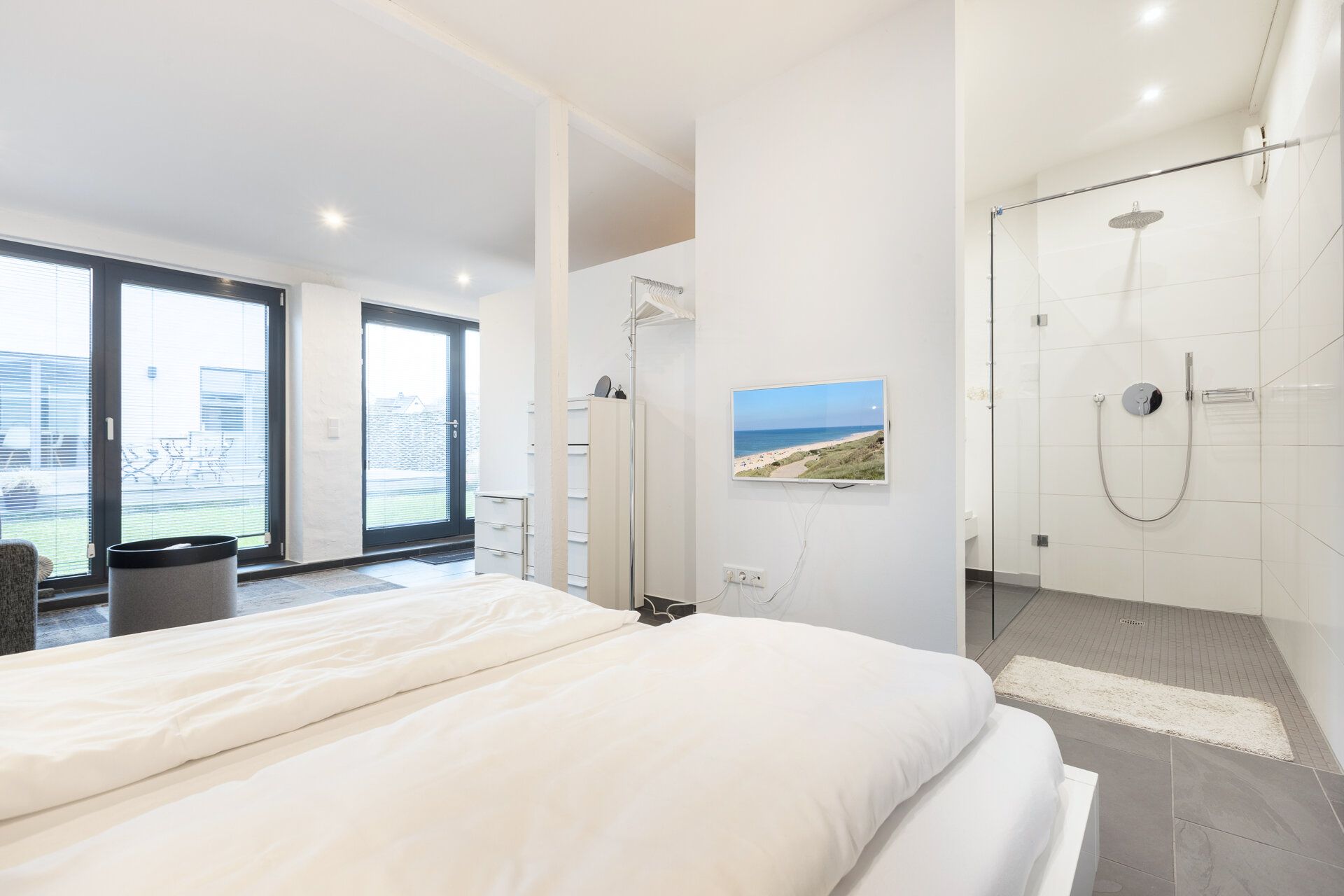 Helles Schlafzimmer mit Doppelbett, Fernseher und offenem Zugang zu einem modernen Duschbad.