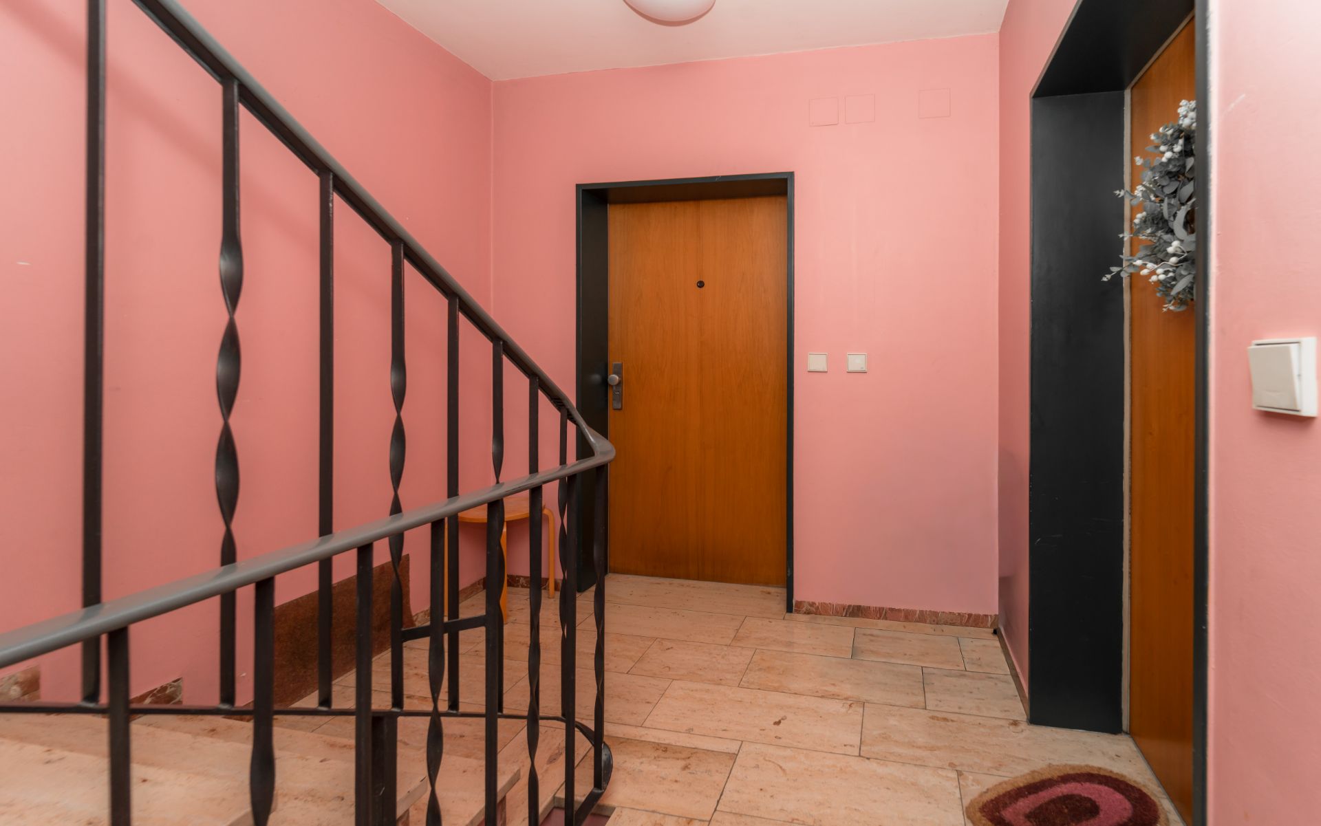 Wohnungseingang mit rosa Wänden, Treppengeländer und Aufzugstür.