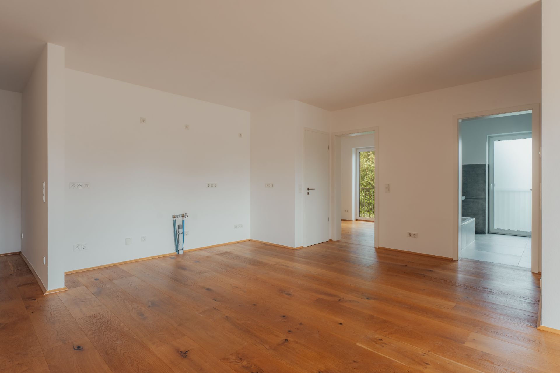 Leerer Raum mit Holzboden, weißen Wänden und Zugang zu einem Badezimmer und einem weiteren Raum.