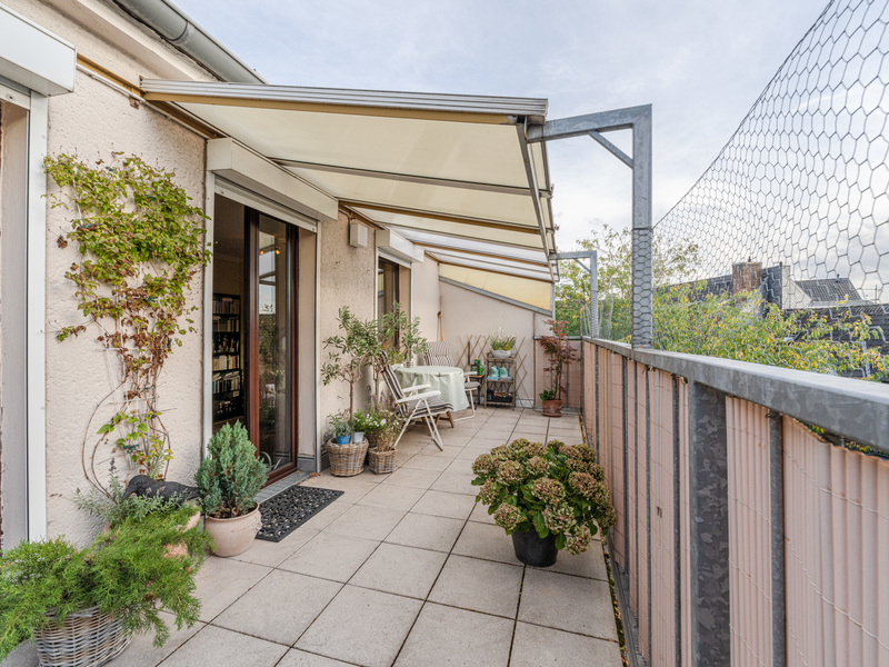 Geräumiger Balkon mit Markise, Pflanzen in Töpfen und einem kleinen Tisch mit Stühlen.
