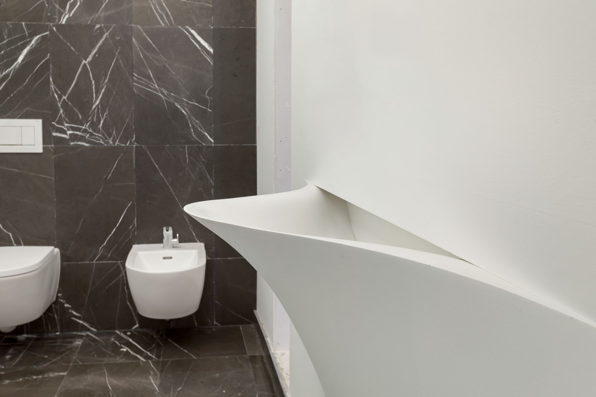 Modernes Badezimmer mit dunklen Fliesen, Bidet und wandhängender Toilette.