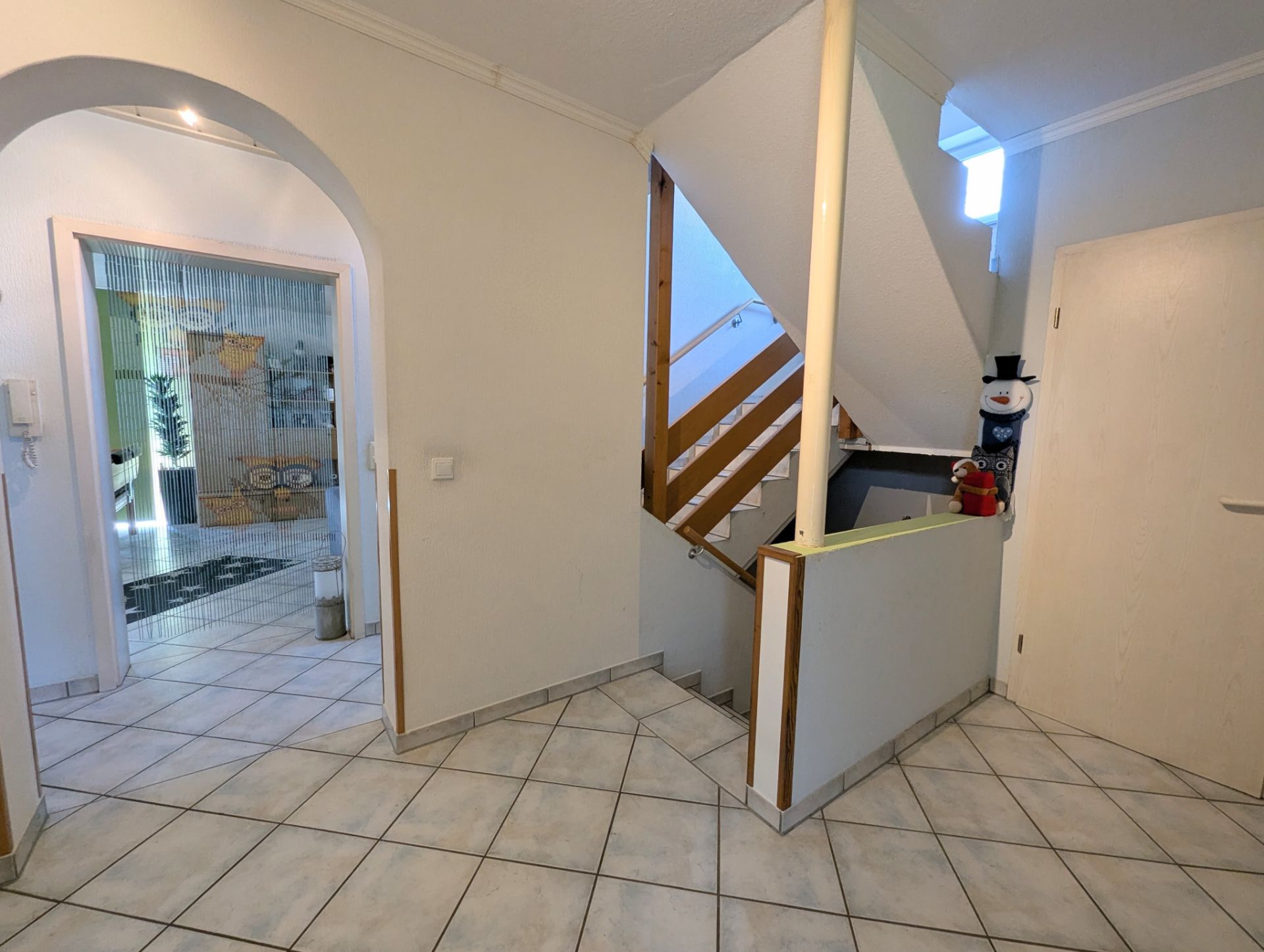Heller Flur mit Fliesenboden, Treppe nach oben und Plüschschneemann auf der Treppe.