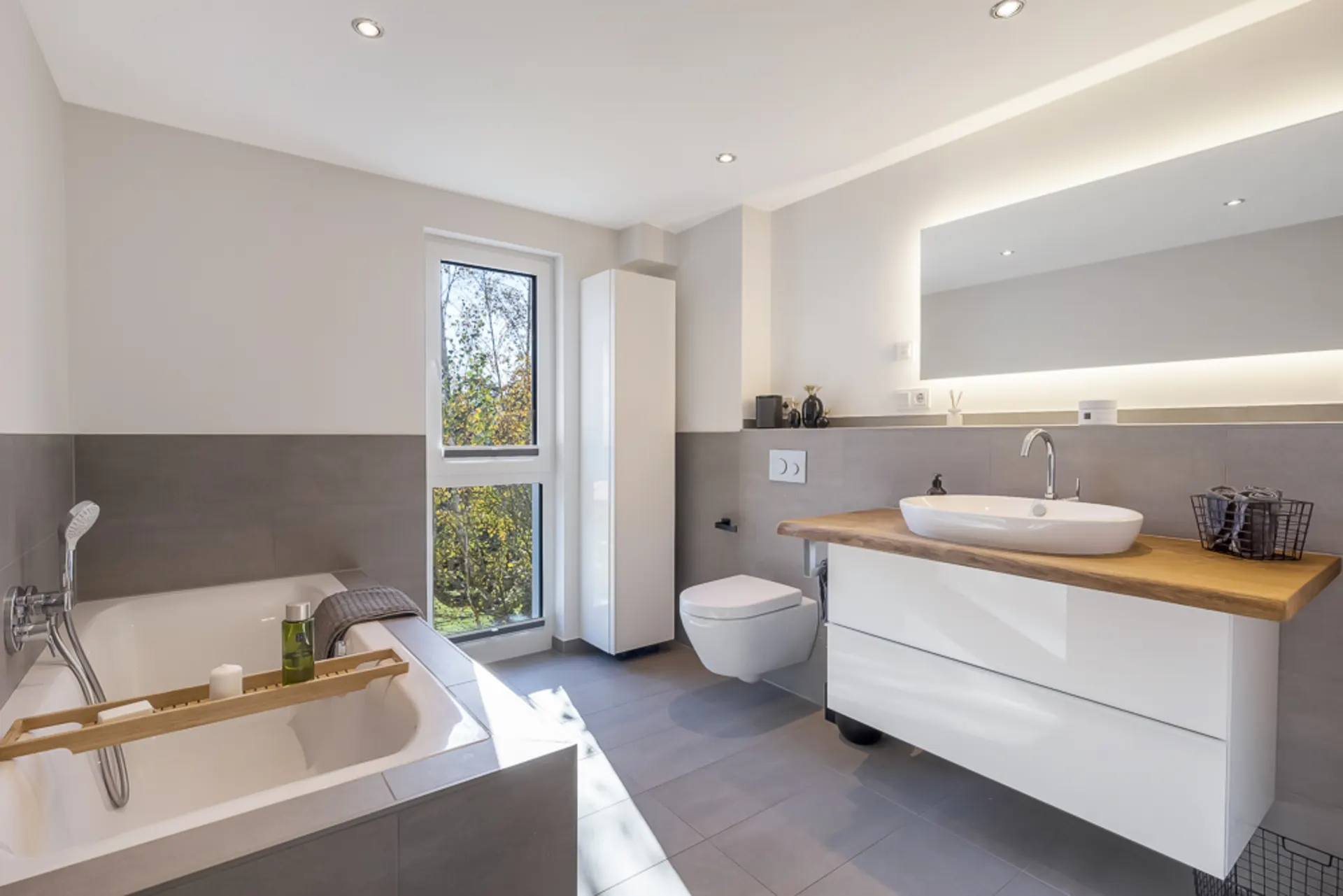 Modernes Badezimmer mit Badewanne, Fenster, Waschbecken, Spiegel und Hängetoilette.