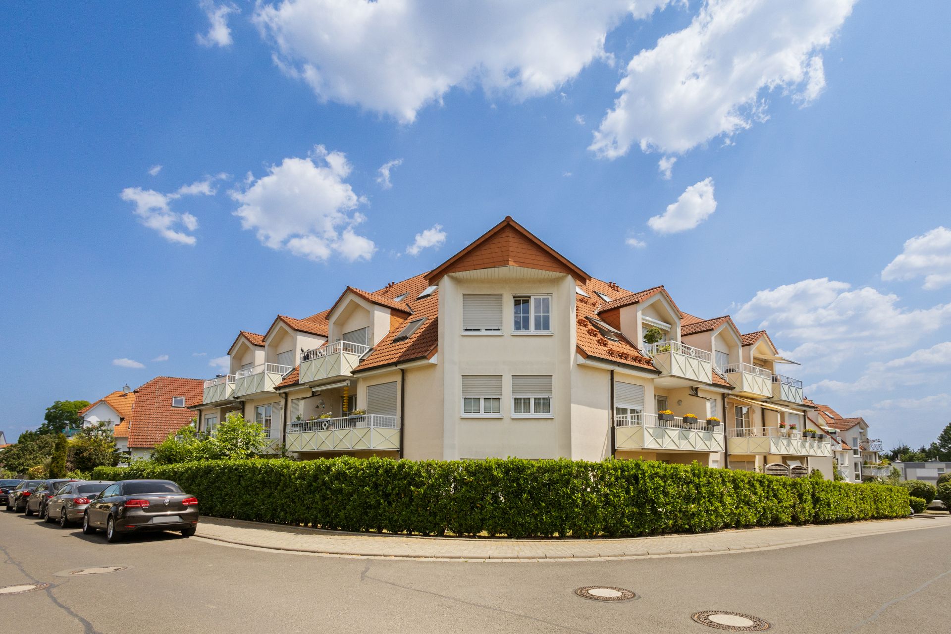 Modernes Mehrfamilienhaus mit Balkonen und rotem Dach an einer Straßenecke.