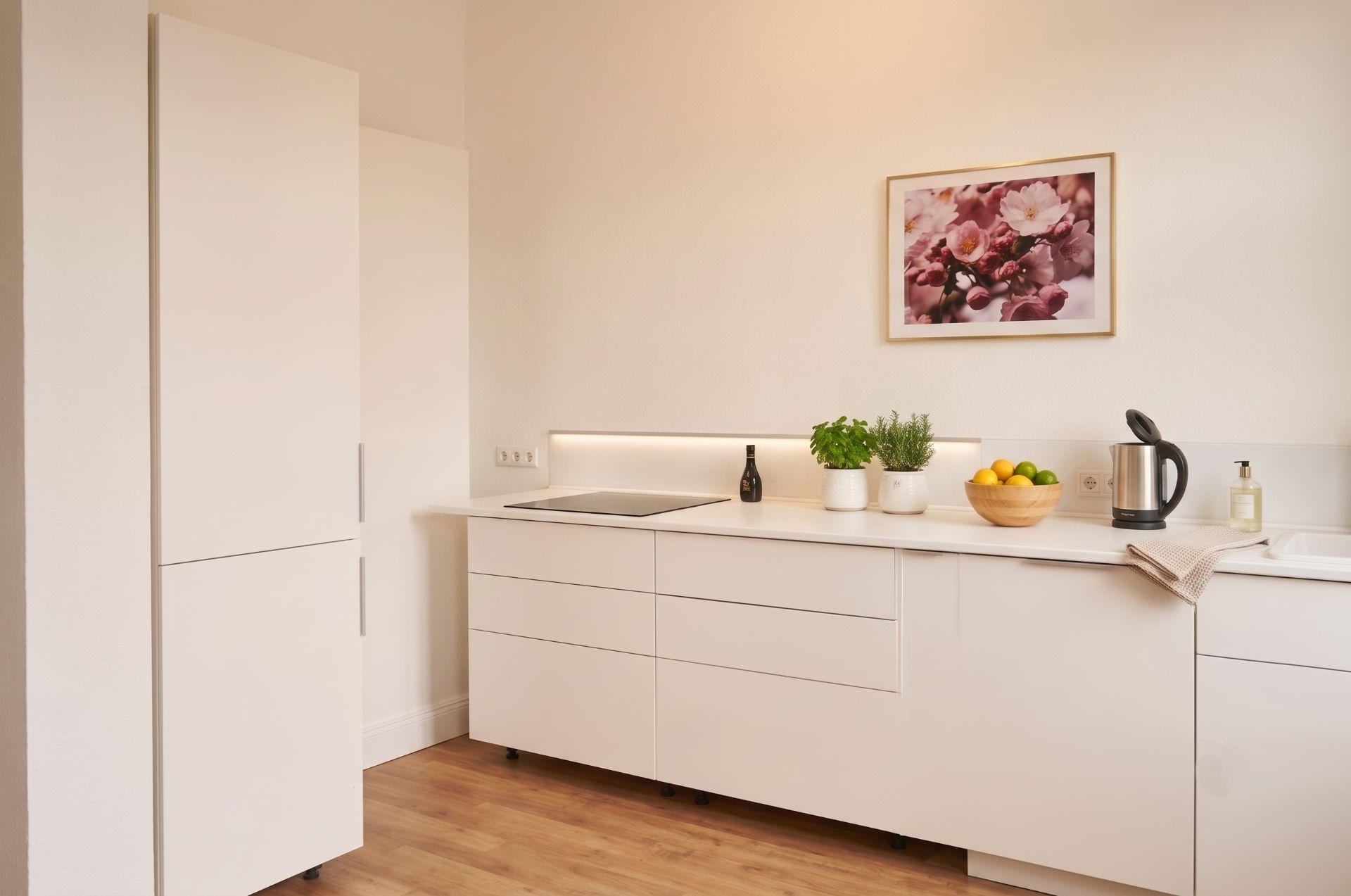 Moderne weiße Küche mit Holzfußboden, Kräutern, Obstschale und Wasserkocher auf der Arbeitsplatte.