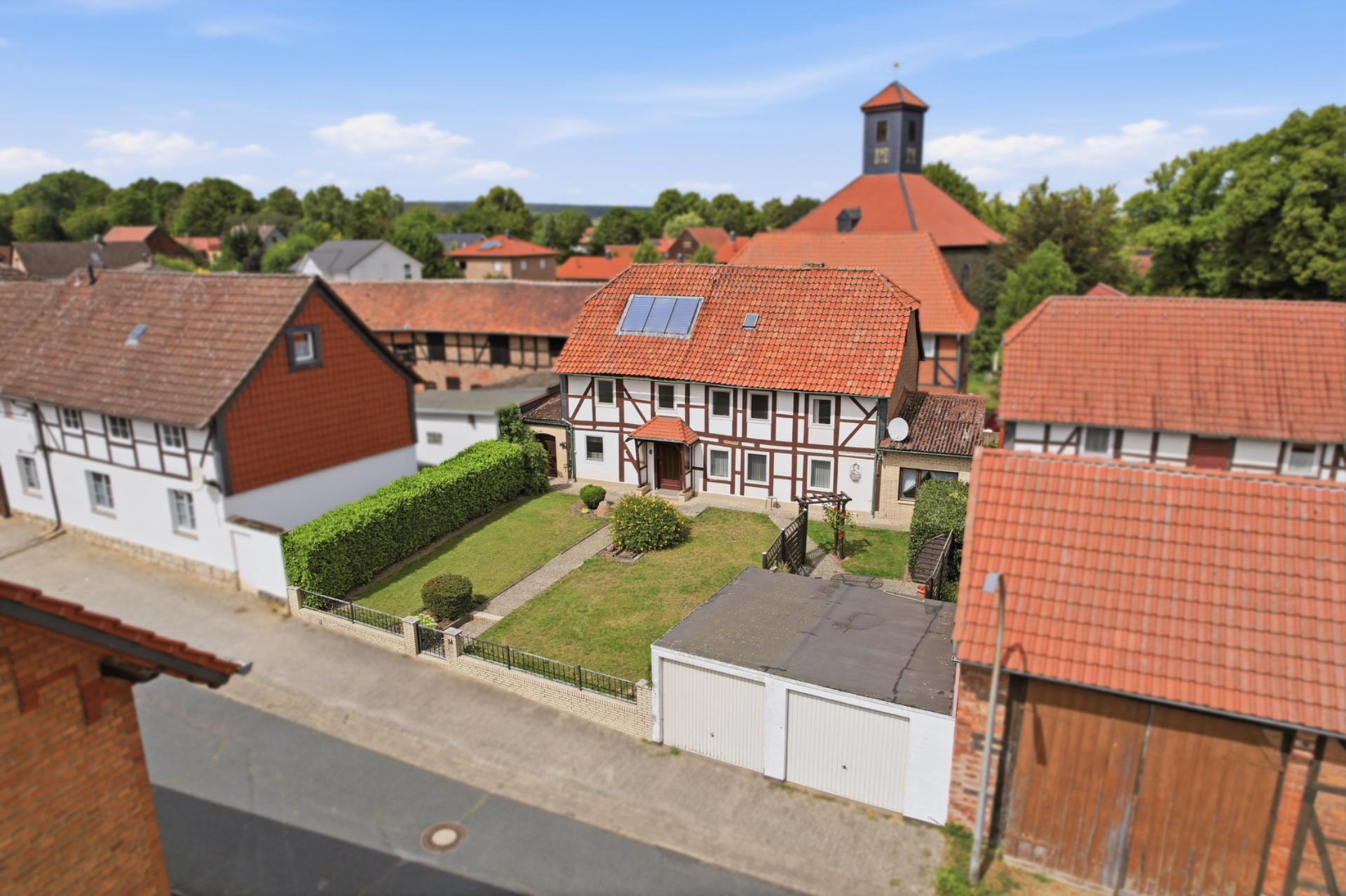 Fachwerkhaus mit rotem Dach, Vorgarten und Doppelgarage, umgeben von weiteren Häusern.