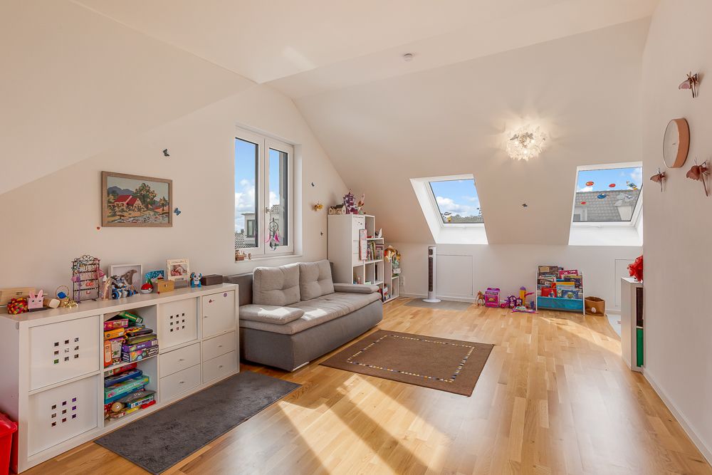 Helles Kinderzimmer mit Sofa, Spielzeugregalen, Holzfußboden und Dachfenstern.