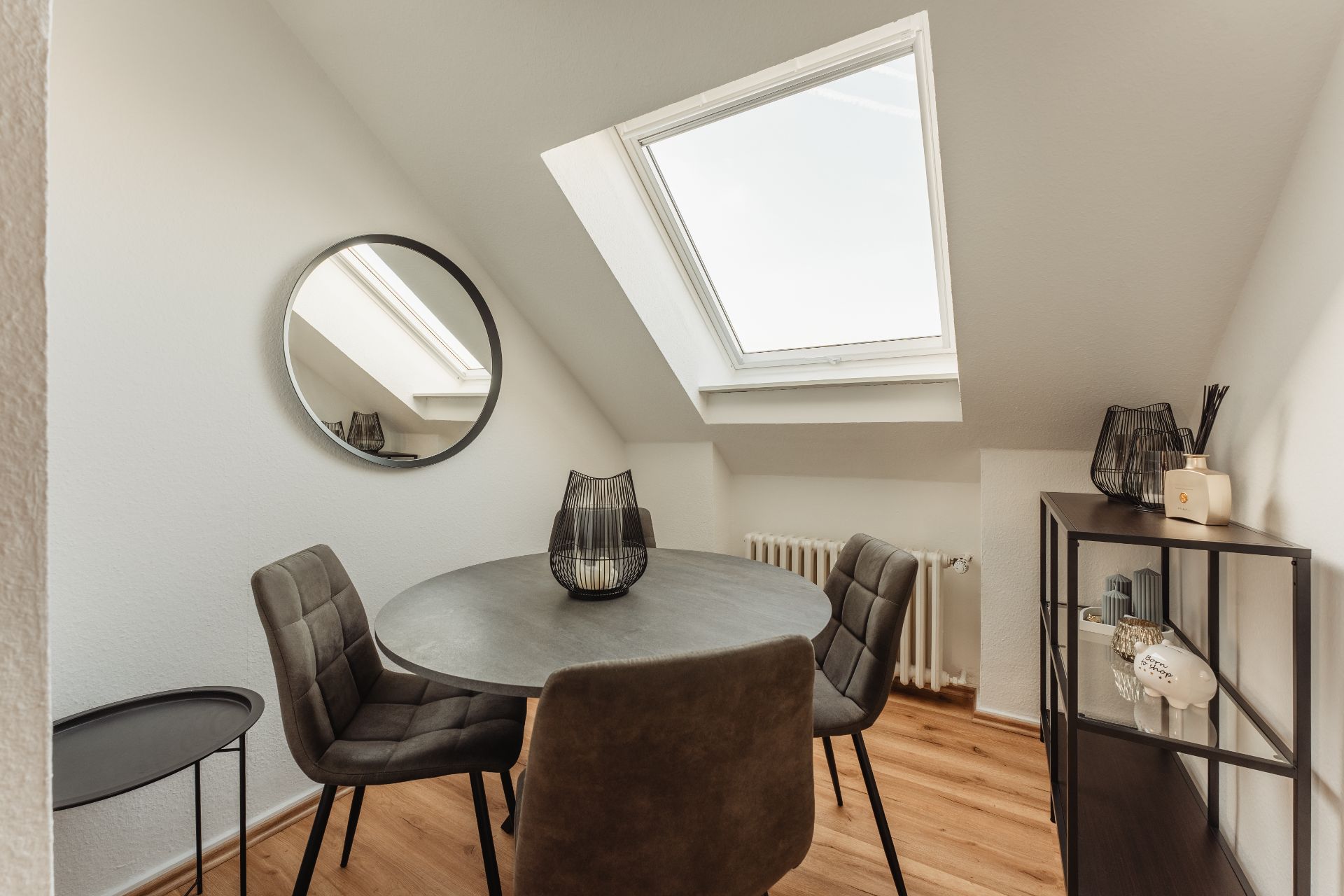 Essbereich mit rundem Tisch, vier Stühlen, Regal, Wandspiegel und Dachfenster.
