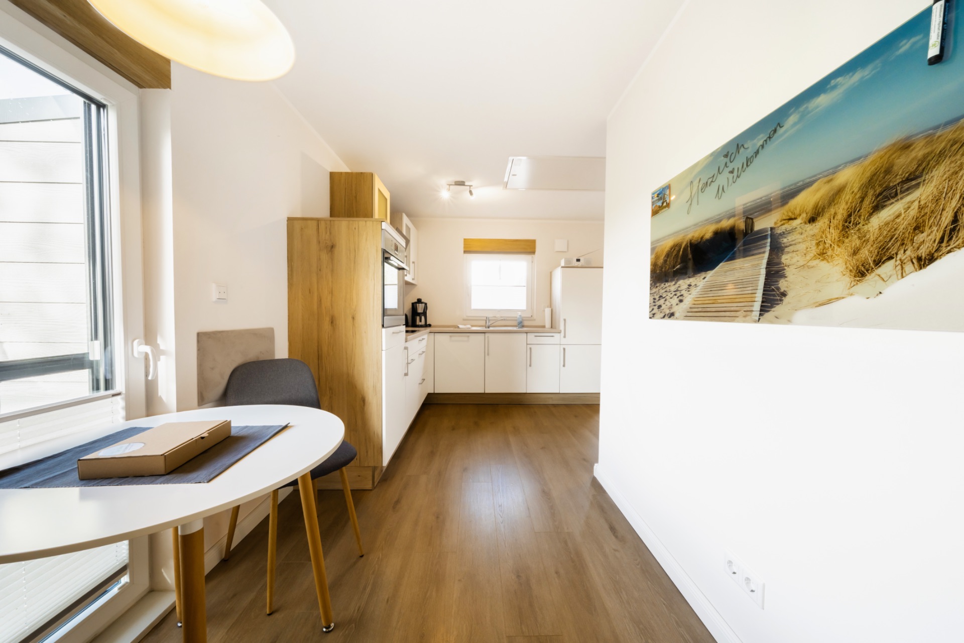 Helle Küche mit Essbereich, Holzfußboden und großem Fenster, modernes Bild an der Wand.