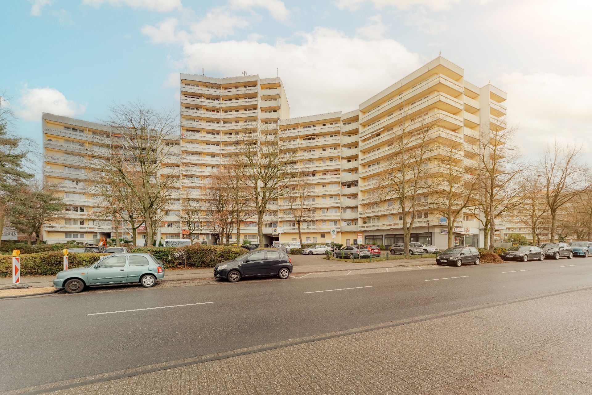 Mehrstöckiges Wohnhaus mit Balkonen und parkenden Autos davor.