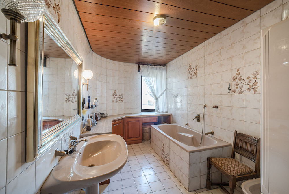 Helles Badezimmer mit Badewanne, Waschbecken, großem Spiegel und Holzdecke.