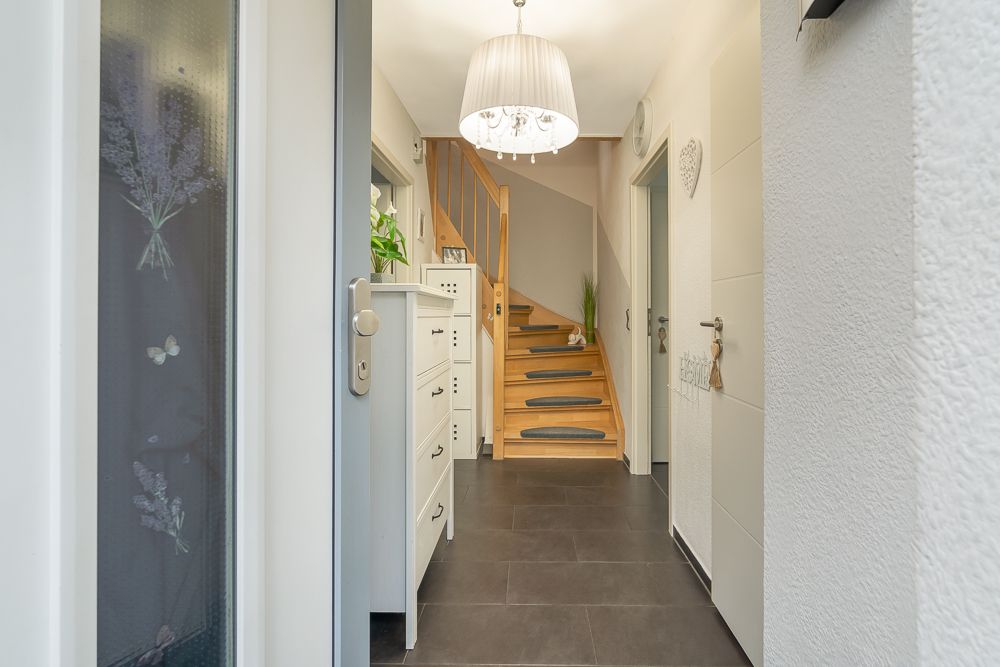 Heller Flur mit Holztreppe, weißen Kommoden und Hängelampe in einem Wohnhaus.