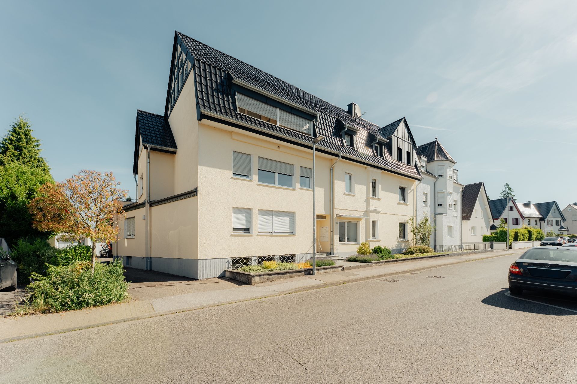 Mehrfamilienhaus mit dunklem Dach und beigen Fassaden an einer ruhigen Wohnstraße.