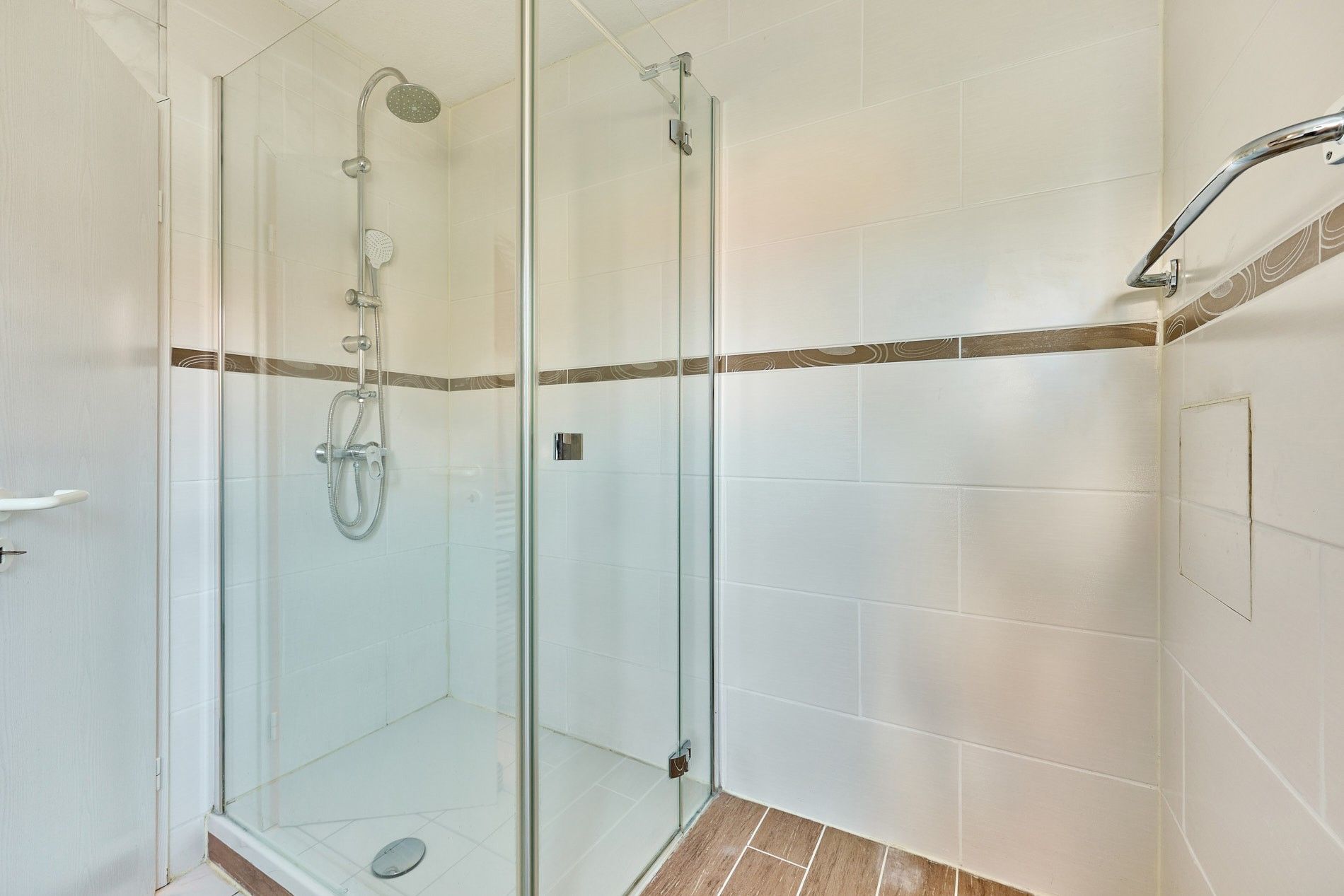 Moderne Dusche mit Glastüren und weißen Fliesen an den Wänden.