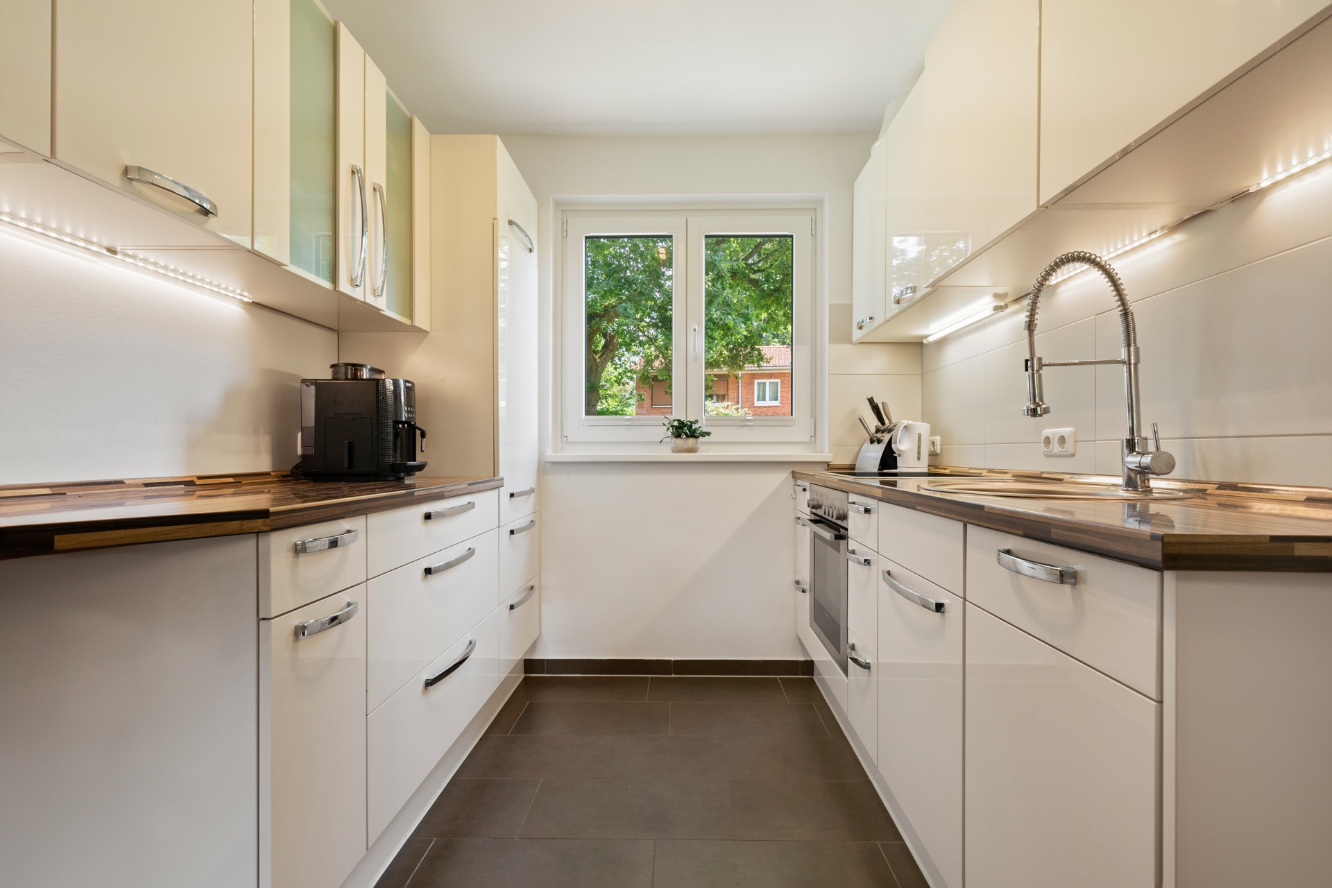 Moderne Küche mit weißen Schränken, Holzarbeitsplatten und großem Fenster in der Mitte.